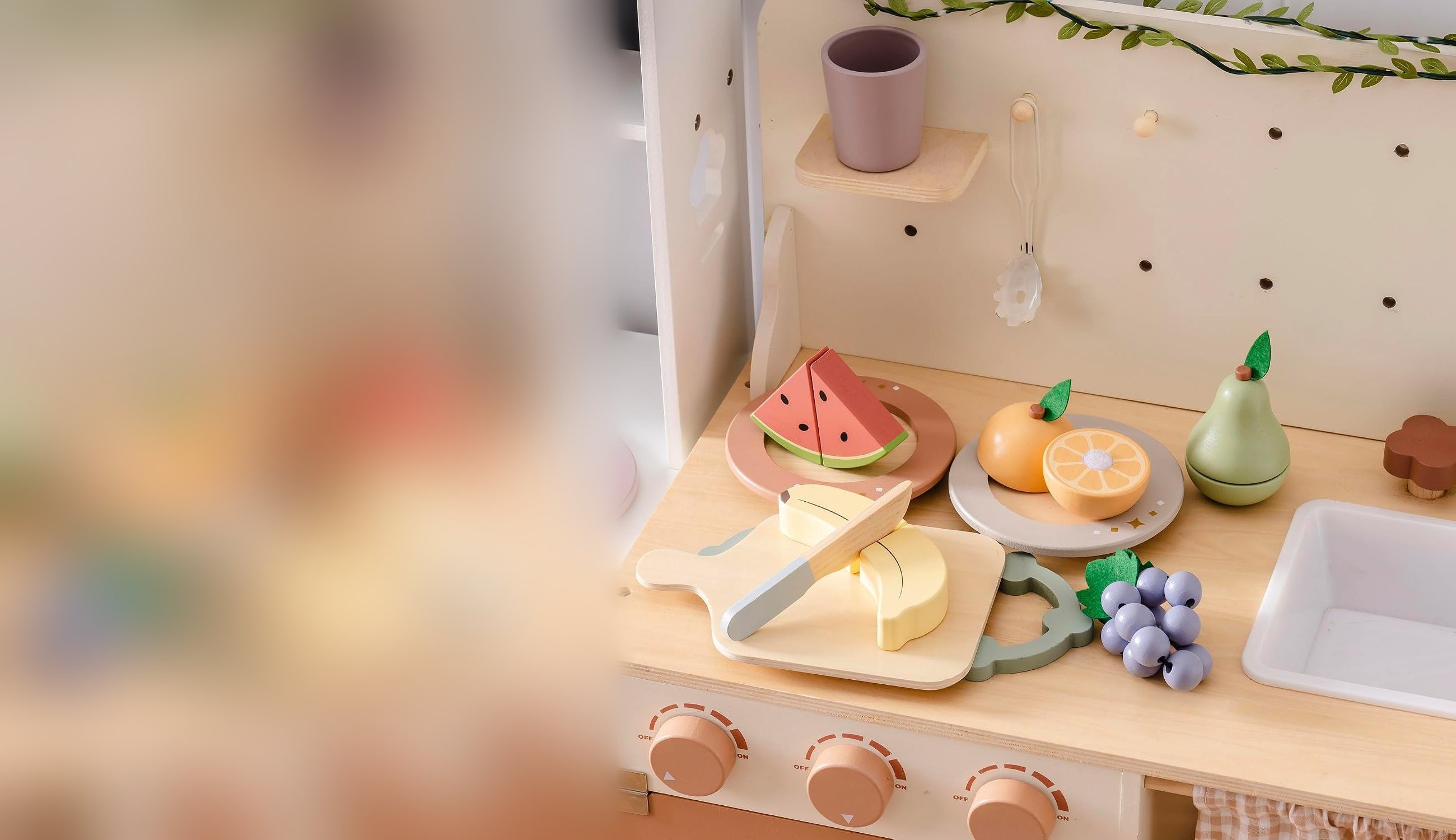 Wooden play fruit on a toy kitchen worktop: watermelon, orange, pear, banana and grapes